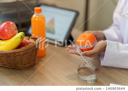 Nutritionist holding orange with measuring tape for healthy eating concept Nutritionist holding orange with measuring tape for healthy eating concept 140903644