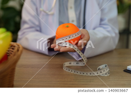 Cropped hands of doctor holding fresh orange with measuring tape for nutrition and weight management Cropped hands of doctor holding fresh orange with measuring tape for nutrition and weight management 140903667