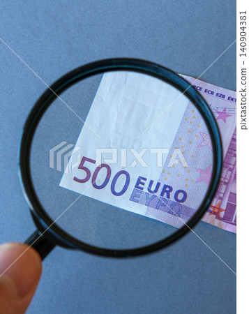 Magnifying Glass Examining 500 Euro Banknote for Counterfeit Detection and Currency Verification Check 140904381