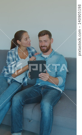 Vertical Video Happy couple renters owners tenants sit on sofa use digital tablet on moving day in new house, man and woman relax on couch with boxes discuss interior design online idea renovate home. Vertical Video Happy couple renters owners tenants sit on sofa use digital tablet on moving day in new house, man and woman relax on couch with boxes discuss interior design online idea renovate home. 140905198