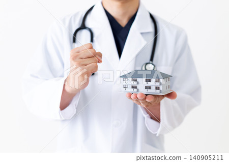 一位身穿白大褂的中年男醫師手持房屋模型,做出勝利的手勢。 一位身穿白大褂的中年男醫師手持房屋模型,做出勝利的手勢。 140905211