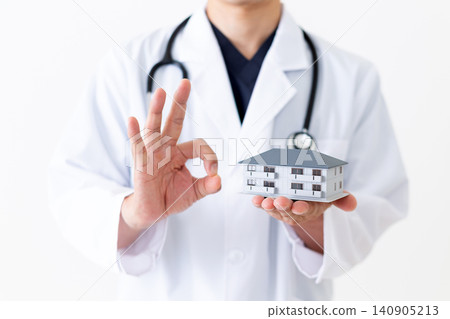 A middle-aged male doctor in a white coat poses in a circle while holding a model of a house. A middle-aged male doctor in a white coat poses in a circle while holding a model of a house. 140905213