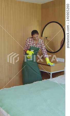 Vertical Video Professional cleaners in uniform washing floor and wiping dust from the furniture in the hotel room or apartment bedroom. Cleaning service concept. Vertical Video Professional cleaners in uniform washing floor and wiping dust from the furniture in the hotel room or apartment bedroom. Cleaning service concept. 140905260