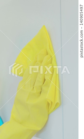 Vertical Video Woman's hand in a yellow rubber glove cleans the shiny surface of a modern plastic kitchen Cabinet with a cloth. The concept of spring cleaning and home work. Vertical Video Woman's hand in a yellow rubber glove cleans the shiny surface of a modern plastic kitchen Cabinet with a cloth. The concept of spring cleaning and home work. 140905497