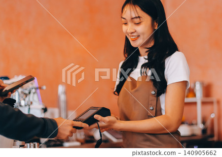 Asian senior female barista adult receiving mobile payment from customer using smartphone at cafe demonstrating modern cashless transaction in cozy local family coffee shop Asian senior female barista adult receiving mobile payment from customer using smartphone at cafe demonstrating modern cashless transaction in cozy local family coffee shop 140905662