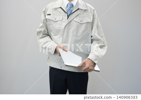 一位身穿工作服的年輕男子拿著筆記型電腦 一位身穿工作服的年輕男子拿著筆記型電腦 140906383