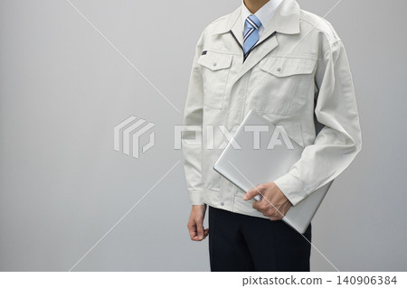 一位身穿工作服的年輕男子拿著筆記型電腦 一位身穿工作服的年輕男子拿著筆記型電腦 140906384