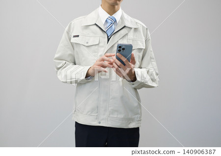 一位身穿工作服的年輕男子手持智慧型手機 一位身穿工作服的年輕男子手持智慧型手機 140906387
