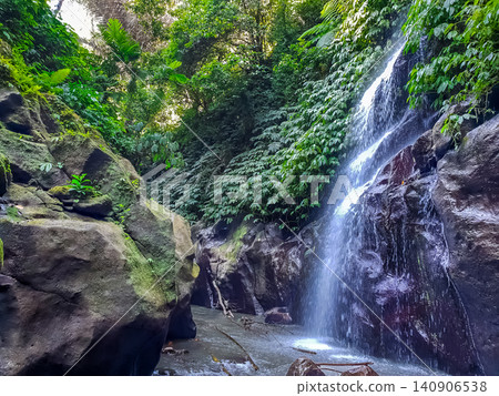 Tropical waterfall cascading over dark mossy rocks into shallow pool surrounded by dense jungle vegetation Tropical waterfall cascading over dark mossy rocks into shallow pool surrounded by dense jungle vegetation 140906538