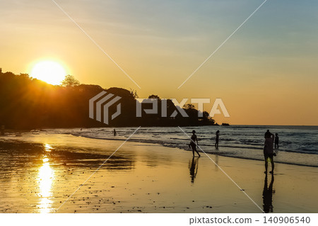 People Silhouetted on Tropical Beach at Golden Sunset with Sun Reflection on Wet Sand People Silhouetted on Tropical Beach at Golden Sunset with Sun Reflection on Wet Sand 140906540