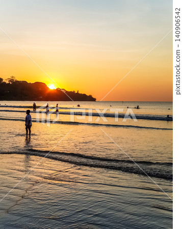 People Silhouetted on Tropical Beach at Golden Sunset with Sun Reflection on Wet Sand 140906542