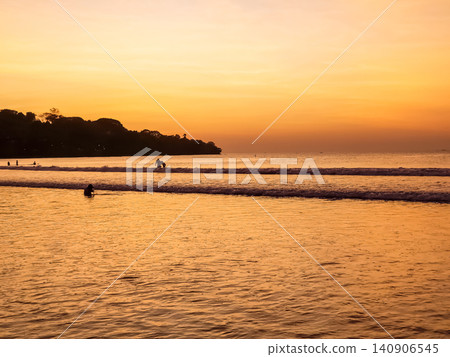 People Swimming in Ocean Waves at Tropical Beach During Vivid Orange Sunset with Tree Silhouette 140906545