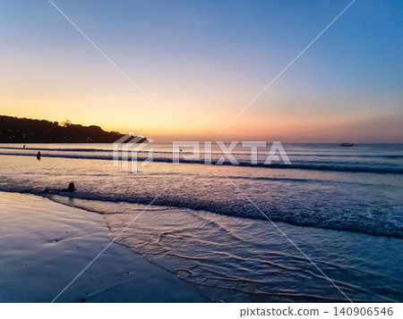 Tropical beach at twilight with orange and blue sunset sky, silhouetted headland and fishing boat on calm ocean Tropical beach at twilight with orange and blue sunset sky, silhouetted headland and fishing boat on calm ocean 140906546