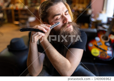 Bearded master leaning back on a leather sofa with a straight razor Bearded master leaning back on a leather sofa with a straight razor 140906962