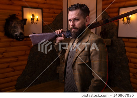 A hunter standing with a shotgun in a cozy log cabin interior 140907050
