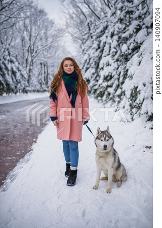 Red-haired girl walking with a husky dog on a snowy forest path Red-haired girl walking with a husky dog on a snowy forest path 140907094