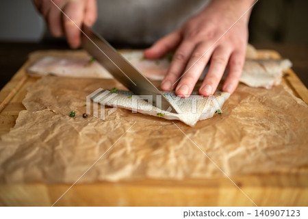 Slicing a seasoned raw fish fillet on a cutting board Slicing a seasoned raw fish fillet on a cutting board 140907123