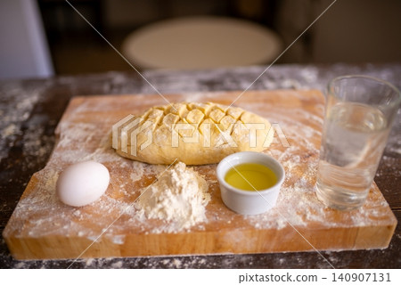 Scored loaf of raw dough with baking ingredients on a board 140907131