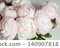 Vertical shot of lush pink peony bouquet with green leaves against neutral grey wall in natural light. 140907818
