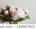 Vertical shot of lush pink peony bouquet with green leaves against neutral grey wall in natural light. 140907822