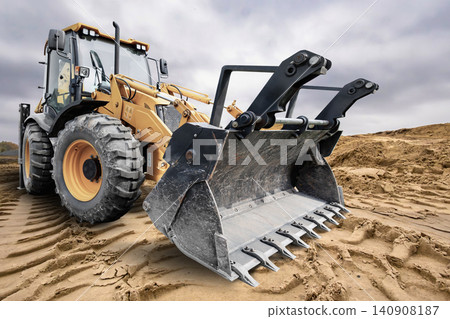 A universal excavator loader is digging into the ground at a construction site with loose soil. The machinery is ready for various tasks A universal excavator loader is digging into the ground at a construction site with loose soil. The machinery is ready for various tasks 140908187