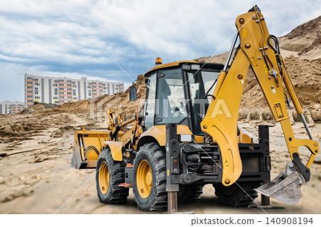 A universal excavator loader is operating on a construction site. It moves earth and prepares the area for new buildings under a cloudy sky A universal excavator loader is operating on a construction site. It moves earth and prepares the area for new buildings under a cloudy sky 140908194