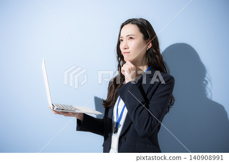 一位日本女商人站在淺藍色背景前,面前擺放著一台筆記型電腦,抬頭望向天空,似乎在思考一些負面的事情。 一位日本女商人站在淺藍色背景前,面前擺放著一台筆記型電腦,抬頭望向天空,似乎在思考一些負面的事情。 140908991