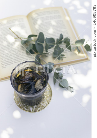 A summer day with dappled sunlight filtering through the trees, iced coffee, and eucalyptus leaves – a table photo of reading time. A summer day with dappled sunlight filtering through the trees, iced coffee, and eucalyptus leaves – a table photo of reading time. 140909795