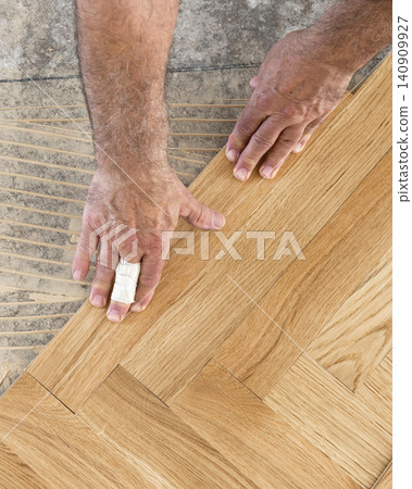 Hands installing herringbone wooden parquet planks during flooring work in apartment renovation Hands installing herringbone wooden parquet planks during flooring work in apartment renovation 140909927
