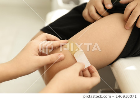 Sister putting sticking plaster onto little brother's leg indoors, closeup Sister putting sticking plaster onto little brother's leg indoors, closeup 140910071