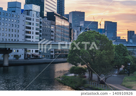 Evening on a riverbank and park in the city, surrounded by skyscrapers. Evening on a riverbank and park in the city, surrounded by skyscrapers. 140910926