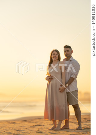 Couple stands together on the beach during sunset while holding hands and enjoying the view Couple stands together on the beach during sunset while holding hands and enjoying the view 140911036