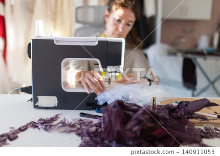 Sewing on a machine while working on fabric scraps in a workshop space during daylight hours Sewing on a machine while working on fabric scraps in a workshop space during daylight hours 140911053