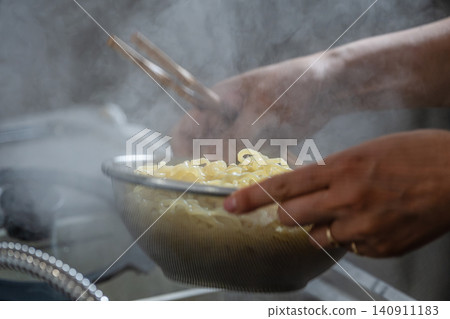 The hands draining the noodles in a colander amidst the steam. The hands draining the noodles in a colander amidst the steam. 140911183
