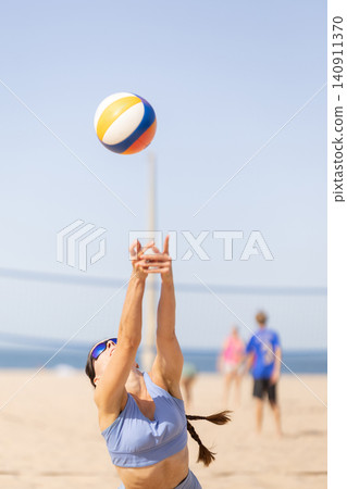Beach volleyball player prepares to set the ball high in the air during a sunny day at the beach with other players in the background Beach volleyball player prepares to set the ball high in the air during a sunny day at the beach with other players in the background 140911370
