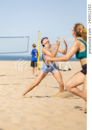 Beach volleyball match takes place under clear sky with athletes competing on warm sand near ocean waves Beach volleyball match takes place under clear sky with athletes competing on warm sand near ocean waves 140911383
