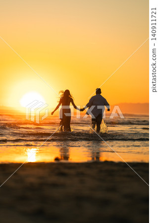 Couple walks hand in hand into the ocean during sunset on a beach Couple walks hand in hand into the ocean during sunset on a beach 140911721