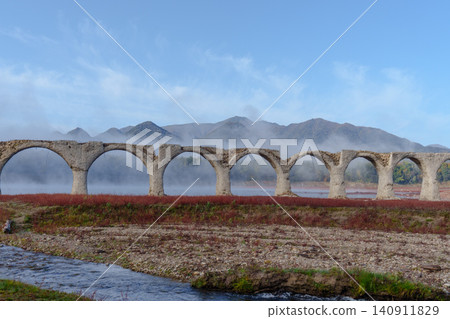 The Taushubetsu River Bridge in Kamishihoro Town, Hokkaido: A spectacular view of the former JNR Shihoro Line with autumn foliage and a clear blue sky. A tourist attraction. The Taushubetsu River Bridge in Kamishihoro Town, Hokkaido: A spectacular view of the former JNR Shihoro Line with autumn foliage and a clear blue sky. A tourist attraction. 140911829