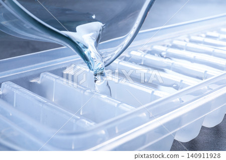 Pouring water into ice cube tray on table, closeup 140911928
