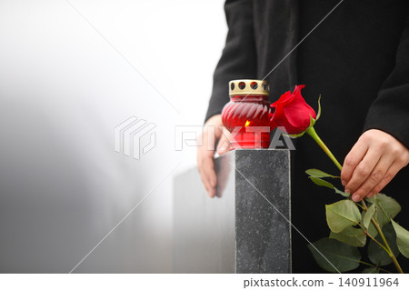 Woman holding red rose near black granite tombstone with candle outdoors, closeup. Funeral ceremony Woman holding red rose near black granite tombstone with candle outdoors, closeup. Funeral ceremony 140911964