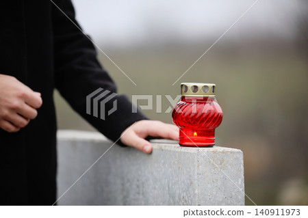 Woman near grey granite tombstone with candle outdoors, closeup. Funeral ceremony Woman near grey granite tombstone with candle outdoors, closeup. Funeral ceremony 140911973