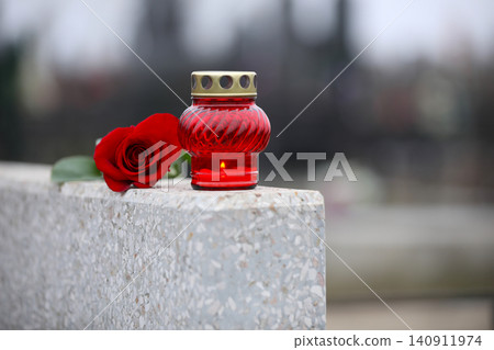 Red rose and candle on light grey granite tombstone outdoors. Funeral ceremony Red rose and candle on light grey granite tombstone outdoors. Funeral ceremony 140911974