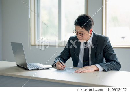一名男子正在筆記型電腦旁填寫文件。 一名男子正在筆記型電腦旁填寫文件。 140912452