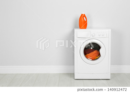 Modern washing machine with laundry and detergent near white wall. Space for text 140912472