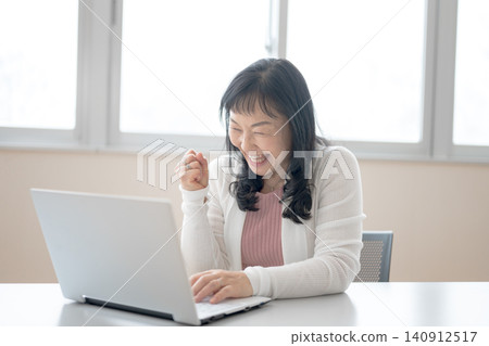 A middle-aged woman makes a triumphant gesture while looking at her computer. A middle-aged woman makes a triumphant gesture while looking at her computer. 140912517