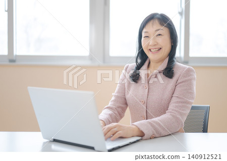 A smiling middle-aged woman working on her laptop. 140912521
