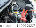 A stock photo of a car helping another car with a dead battery; jumper cables are connected to the battery. 140912837