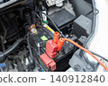 A stock photo of a car helping another car with a dead battery; jumper cables are connected to the battery. 140912840