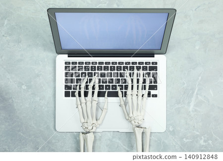 Human skeleton using laptop at grey marble table, top view Human skeleton using laptop at grey marble table, top view 140912848