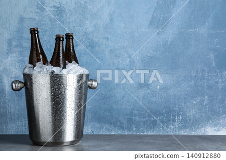 Beer in metal bucket with ice on grey table against light blue background. Space for text Beer in metal bucket with ice on grey table against light blue background. Space for text 140912880